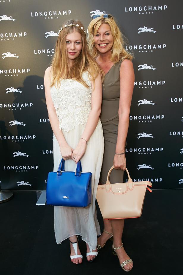 Zwei Frauen posieren mit Longchamp-Handtaschen vor einer Longchamp-Logowand.