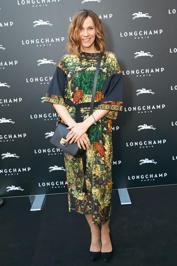 Eine Frau in einem gemusterten Kleid posiert vor einer Longchamp-Wand.