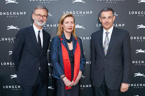 Drei Personen posieren vor einer Wand mit dem Longchamp-Logo.
