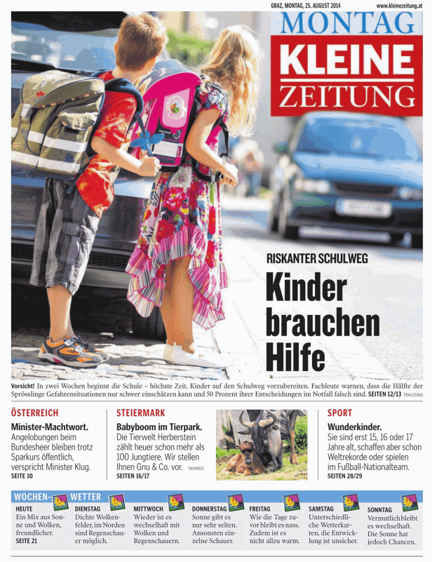 Zwei Kinder mit Schulranzen stehen an einer Straße.