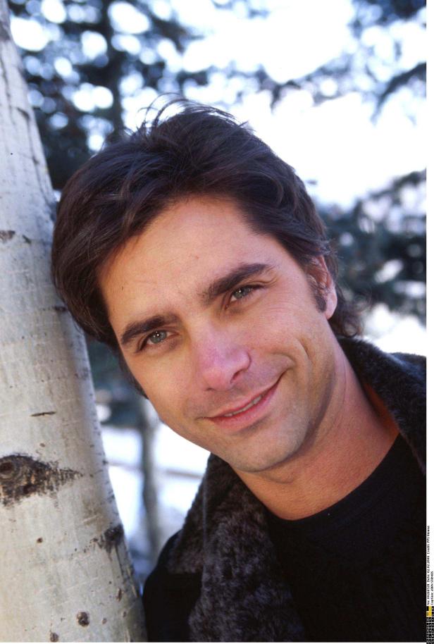 Ein Porträt von John Stamos, der an einem Baum lehnt.