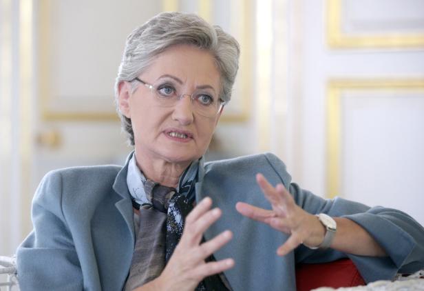 Eine Frau mit Brille und grauem Haar gestikuliert während eines Gesprächs.