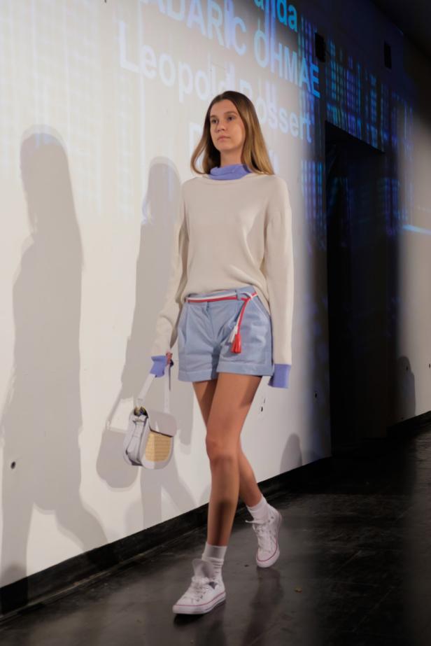 afa awards Eine Frau präsentiert Mode mit Shorts, Pullover und einer kleinen Handtasche auf einem Laufsteg.