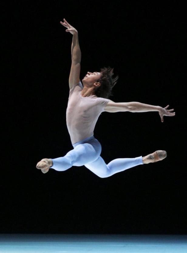 Ein männlicher Balletttänzer springt auf einer Bühne.