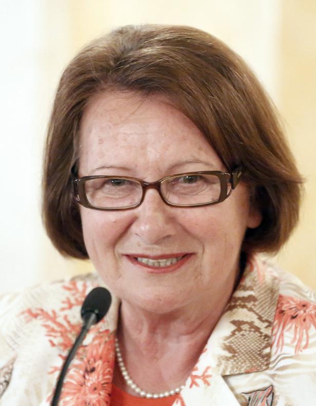 Eine lächelnde Frau mit Brille und kurzem braunen Haar spricht in ein Mikrofon.