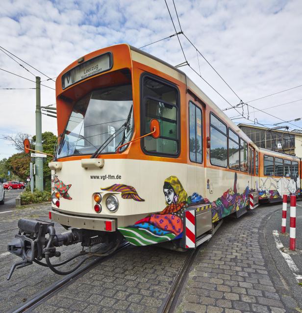 Eine Straßenbahn mit farbenfrohen Graffiti-Motiven steht auf einem Gleis.