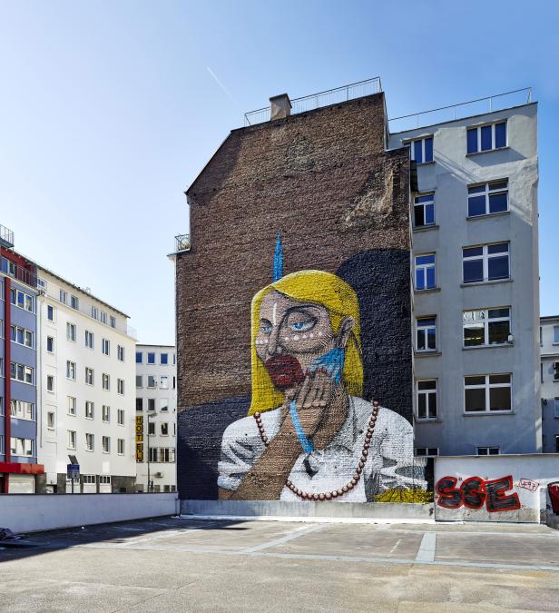 Ein großes Wandgemälde einer Frau mit blonden Haaren und blauem Schmuck auf einem Gebäude.