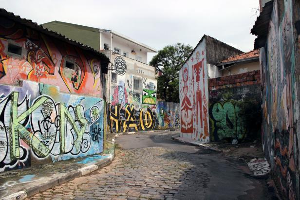 Eine Gasse mit Kopfsteinpflaster, gesäumt von Mauern mit Graffiti und Wandmalereien.