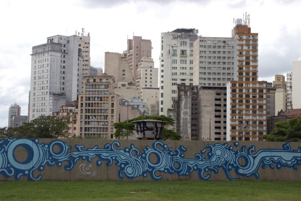 Eine Betonmauer mit blauer Graffiti-Kunst vor einer Skyline von Hochhäusern.