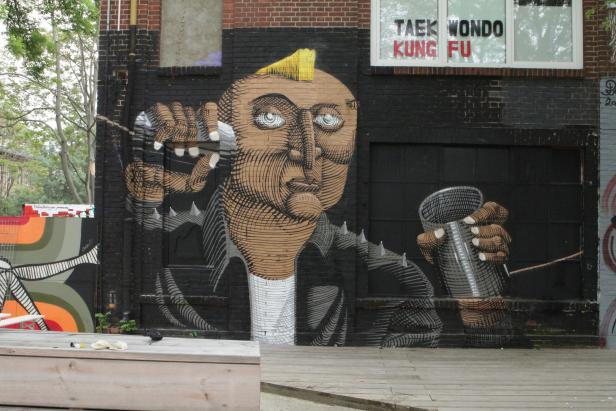 Ein Graffito zeigt ein Gesicht mit Irokesenschnitt, das einen Becher hält.