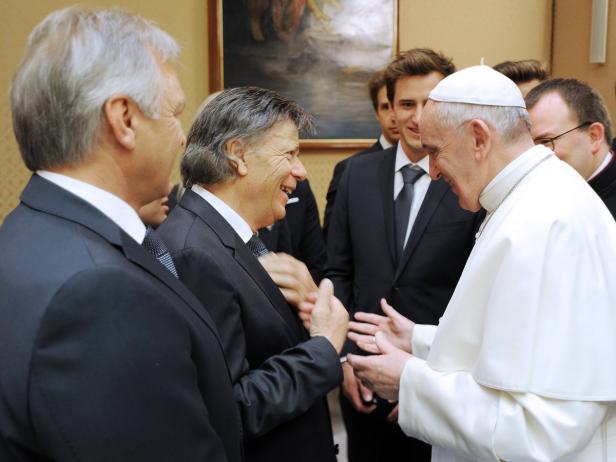 Papst Franziskus begrüßt eine Gruppe von Männern in Anzügen.