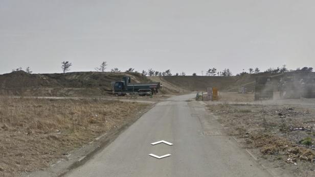 Eine Straße führt zu einer Baustelle mit mehreren Muldenkippern.