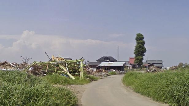 Ein Weg führt durch eine zerstörte japanische Stadt, möglicherweise nach einer Naturkatastrophe.