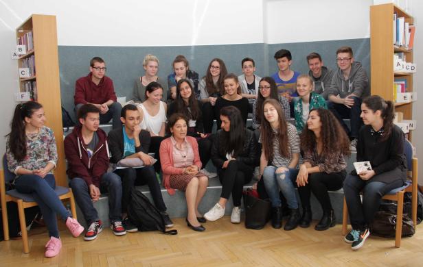 Eine Gruppe von Schülern sitzt mit einer Lehrerin in einem Raum mit Bücherregalen.