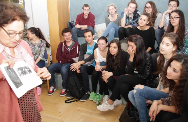 Eine ältere Frau zeigt einer Gruppe von Jugendlichen ein historisches Foto.