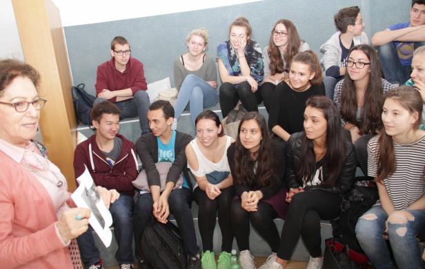 Eine Lehrerin hält ein Foto vor einer Gruppe von Schülern.