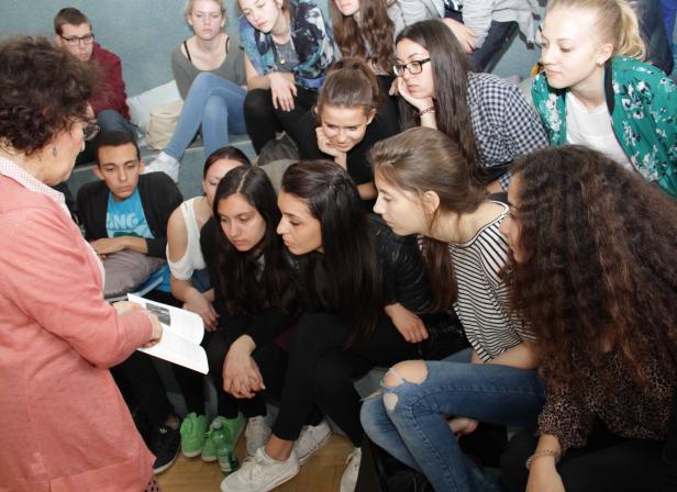 Eine ältere Frau liest einer Gruppe junger Leute aus einem Buch vor.