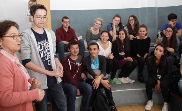 Eine ältere Frau spricht vor einer Gruppe von Teenagern, die auf einer Treppe sitzen.