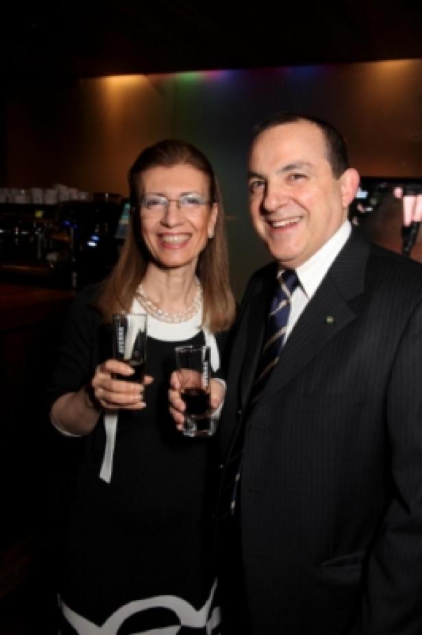Ein Mann im Anzug und eine Frau im Kleid halten Gläser und lächeln.