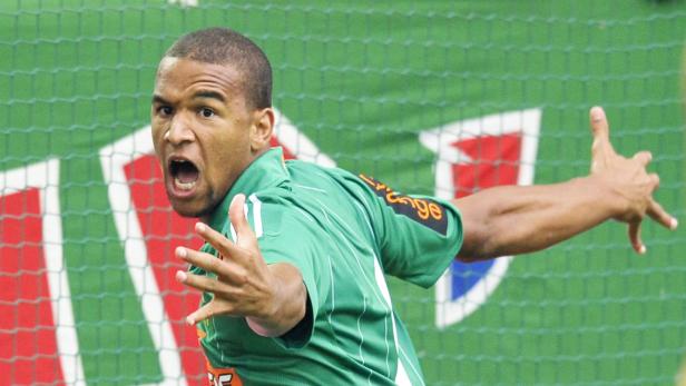 Ein Fußballspieler in einem grünen Trikot jubelt mit geöffnetem Mund und ausgestreckten Armen.