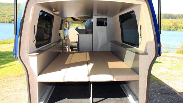 Innenansicht eines umgebauten Lieferwagens mit Bett und Blick auf einen See.