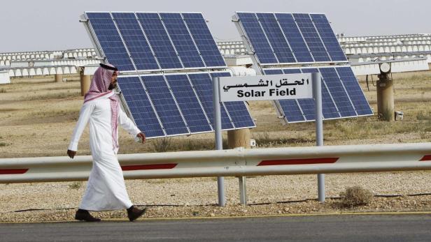 File photo of a Saudi man walking on a street past Ein Mann in traditioneller Kleidung geht an einem Solarpark vorbei.
