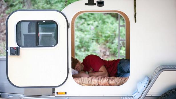 Ein Mann schläft in einem kleinen Wohnwagen.