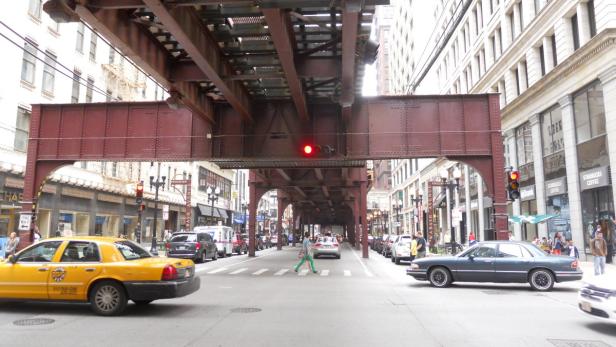 Eine belebte Straße in einer Stadt mit einer erhöhten Bahnbrücke.