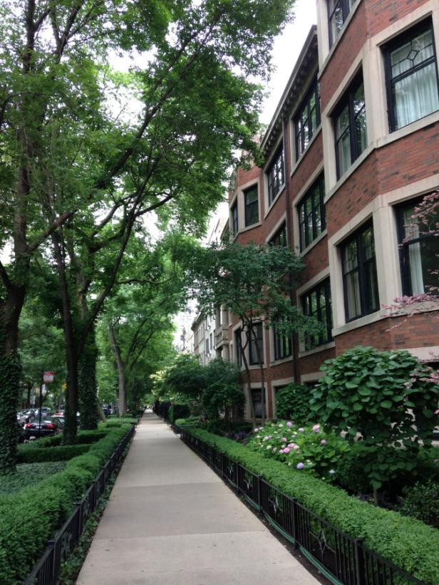 Ein Gehweg führt an gepflegten Gärten und Wohnhäusern vorbei.