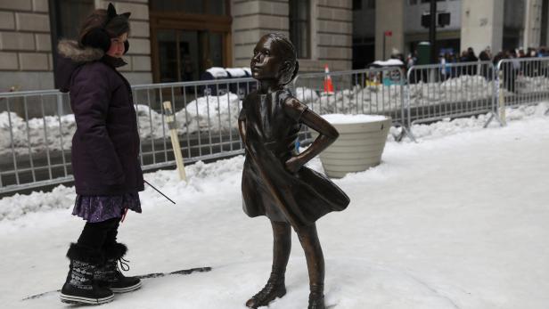 A girl looks at the 'Fearless Girl' statue which s