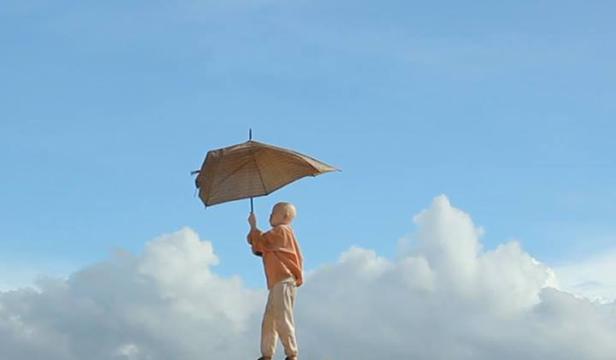 Ein Kind steht vor einem blauen Himmel und hält einen Sonnenschirm.