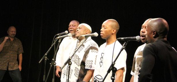 Eine Gruppe von Sängern tritt auf einer Bühne vor einem dunklen Hintergrund auf.