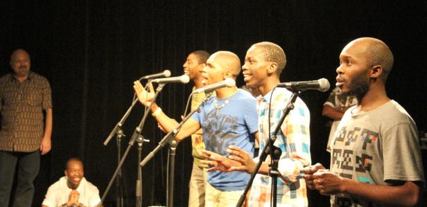 Eine Gruppe von Sängern tritt auf einer Bühne vor einem dunklen Hintergrund auf.