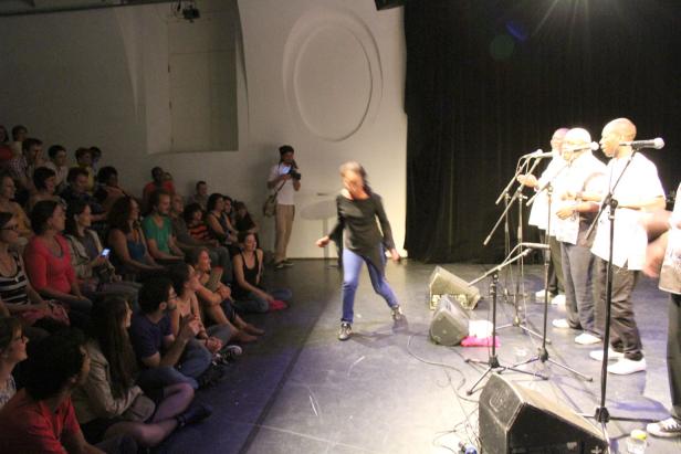 Eine Frau tanzt auf einer Bühne vor einem Publikum und einer Musikgruppe.