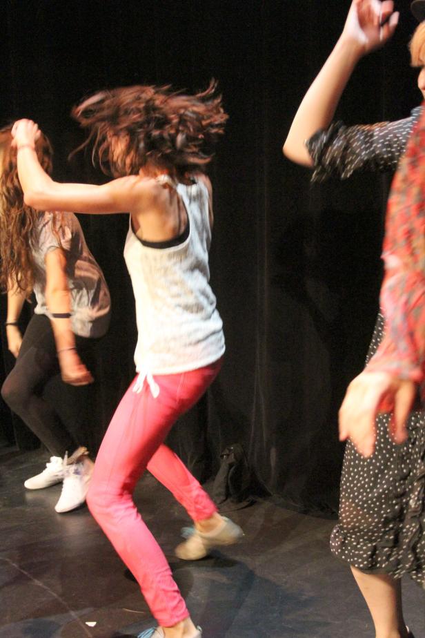 Drei Tänzerinnen führen eine dynamische Choreografie auf einer Bühne auf.