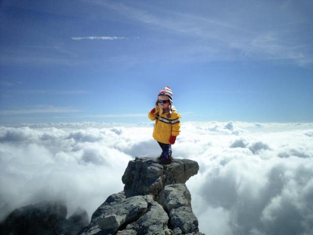 Ein Kind steht auf einem Felsen über den Wolken.