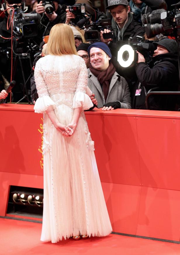 Eine Frau in einem weißen Kleid steht vor einer Gruppe von Fotografen auf einem roten Teppich.
