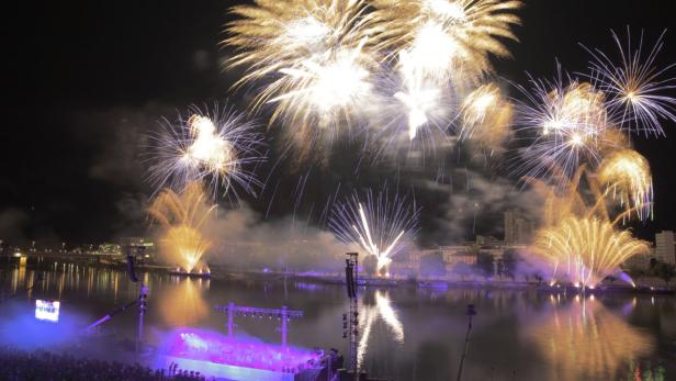 Ein Feuerwerk erhellt den Nachthimmel über einem Fluss.