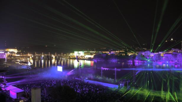 Eine Lasershow beleuchtet eine Menschenmenge an einem Flussufer bei Nacht.