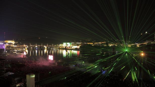 Eine Menschenmenge genießt eine Lasershow am Flussufer bei Nacht.