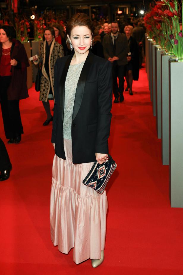 Eine Frau in einem schwarzen Blazer und einem langen, rosa Rock auf einem roten Teppich.