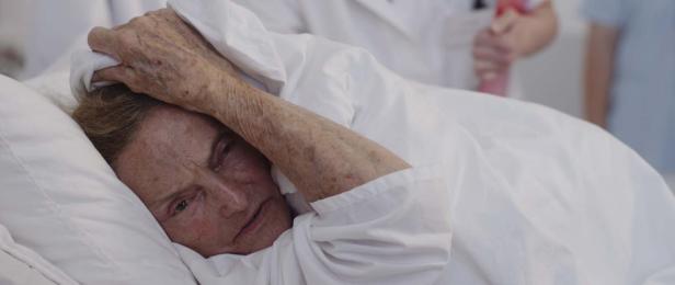 Eine ältere Frau liegt mit schmerzverzerrtem Gesicht im Krankenhausbett.