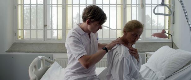 Ein junger Pfleger betreut eine ältere Patientin im Krankenbett.