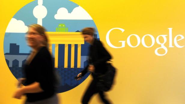 Zwei Personen gehen an einem Google-Logo mit Berliner Wahrzeichen vorbei.