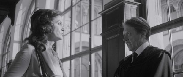 Eine Frau und ein Mann in Robe stehen in einem Gebäude mit großen Fenstern.