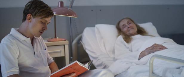 Ein junger Mann liest einer älteren Dame im Krankenbett vor.
