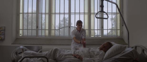 Eine Krankenschwester kümmert sich um einen älteren Patienten, der in einem Krankenhausbett liegt.