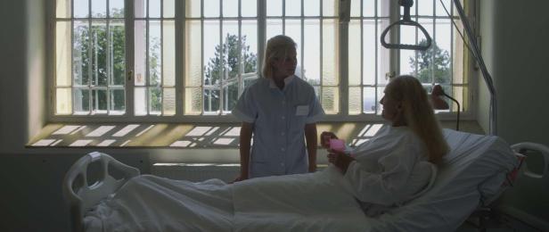 Eine Krankenschwester spricht mit einer älteren Patientin, die in einem Krankenbett liegt.