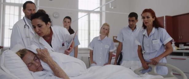 Ärzte und Pflegepersonal stehen um das Bett einer älteren Patientin im Krankenhaus.