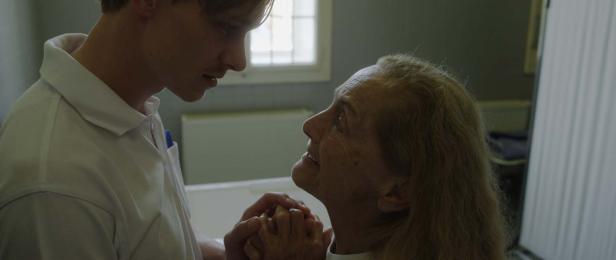 Ein junger Pfleger hält die Hand einer älteren Patientin.